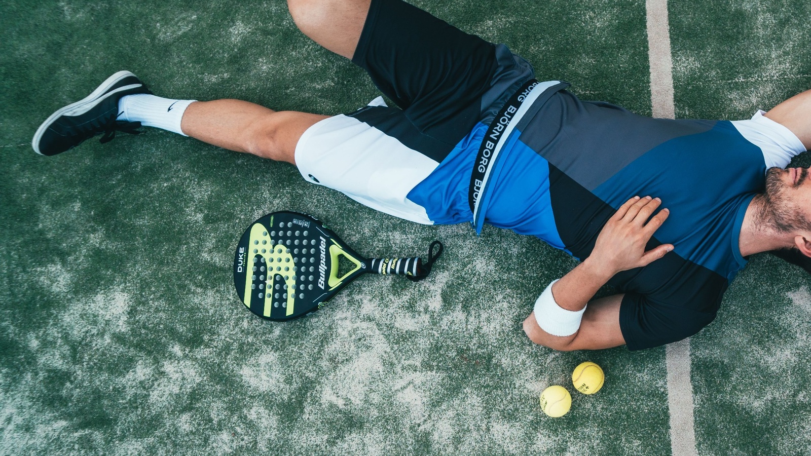 Cam duvarlarla çevrili bir padel kortu ve padel raketi
