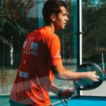 Cam duvarlı padel sahasında alttan servise hazırlanan oyuncu