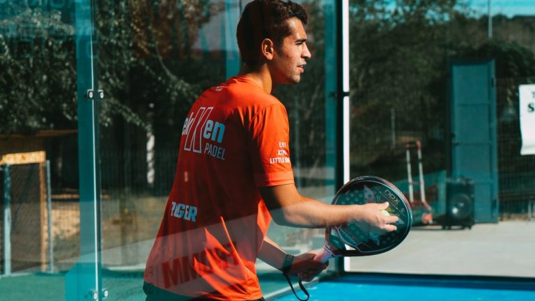 Cam duvarlı padel sahasında alttan servise hazırlanan oyuncu