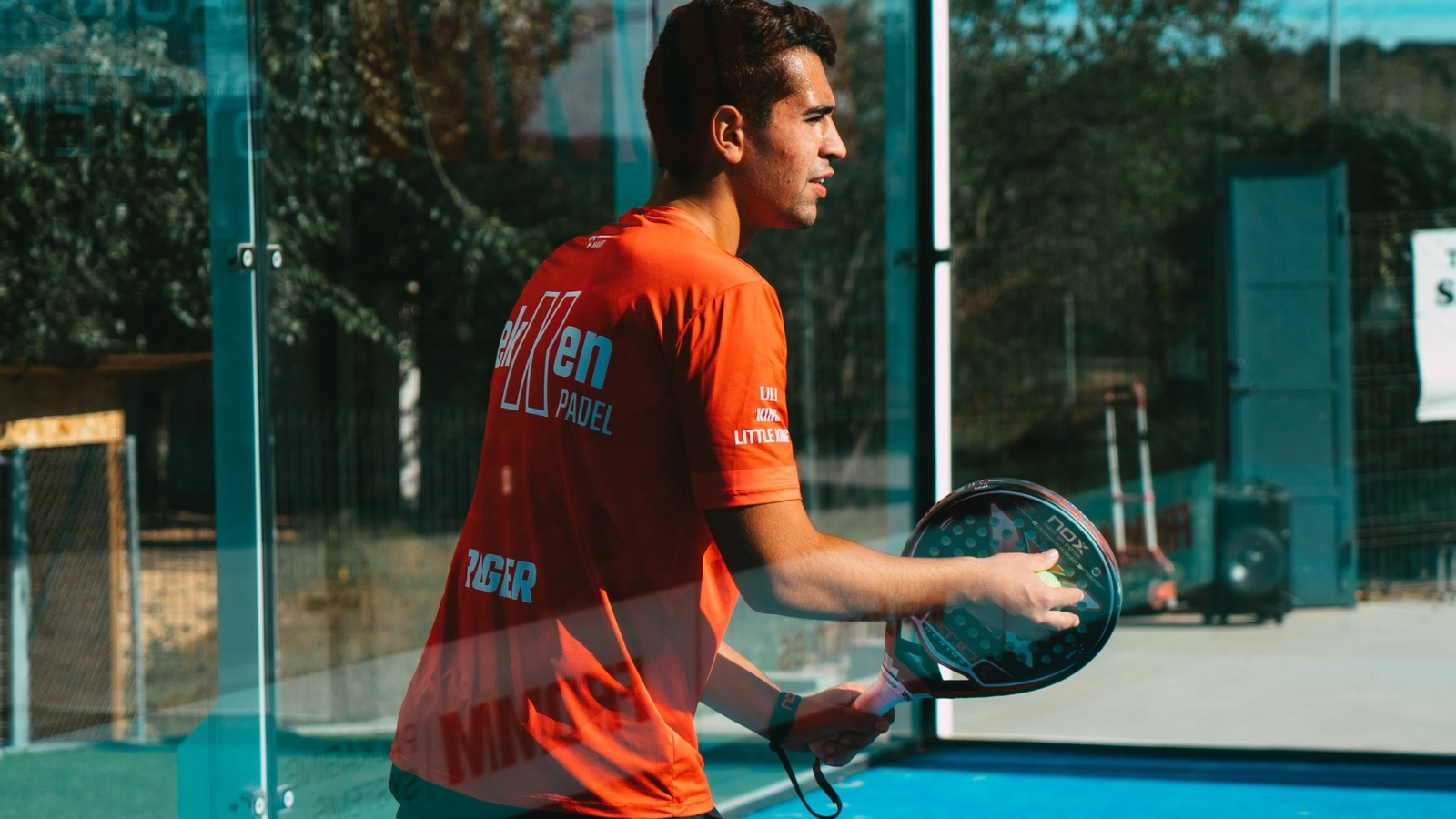 Spieler bereitet sich auf einem Padel-Court mit Glaswänden auf den Aufschlag von unten vor