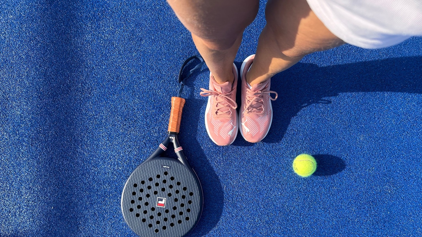 Padelschläger, Handgelenkschlaufe, Courtschuh und Padelball auf einem blauen Court