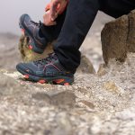 Kayalık zeminde oturup trekking ayakkabısının bağcığını düzelten yürüyüşçü