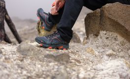 Kayalık zeminde oturup trekking ayakkabısının bağcığını düzelten yürüyüşçü