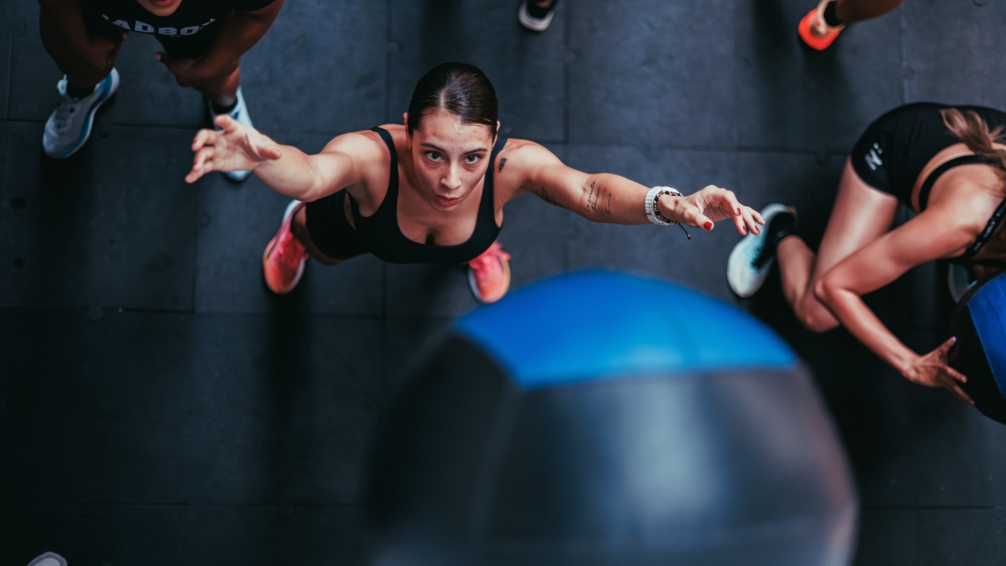 Athlete doing burpees on the floor in a group gym class, wearing running shoes