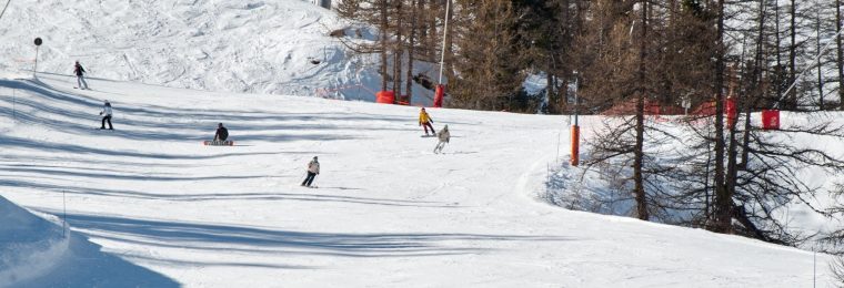 Karlı dağ pistinde aşağı inen kayakçılar ve snowboardcular