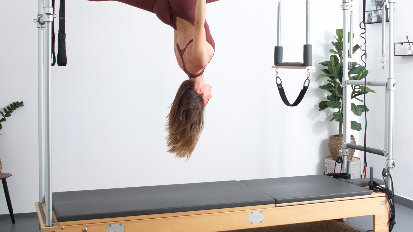Pilates stüdyosunda yay ve kayış düzenekli reformer cihazında ters pozisyonda çalışan kadın