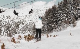 Buzul kayağı sezonunda karlı pistte duran kayakçı ve arkasında ormanın üzerinden geçen telesiyej hattı