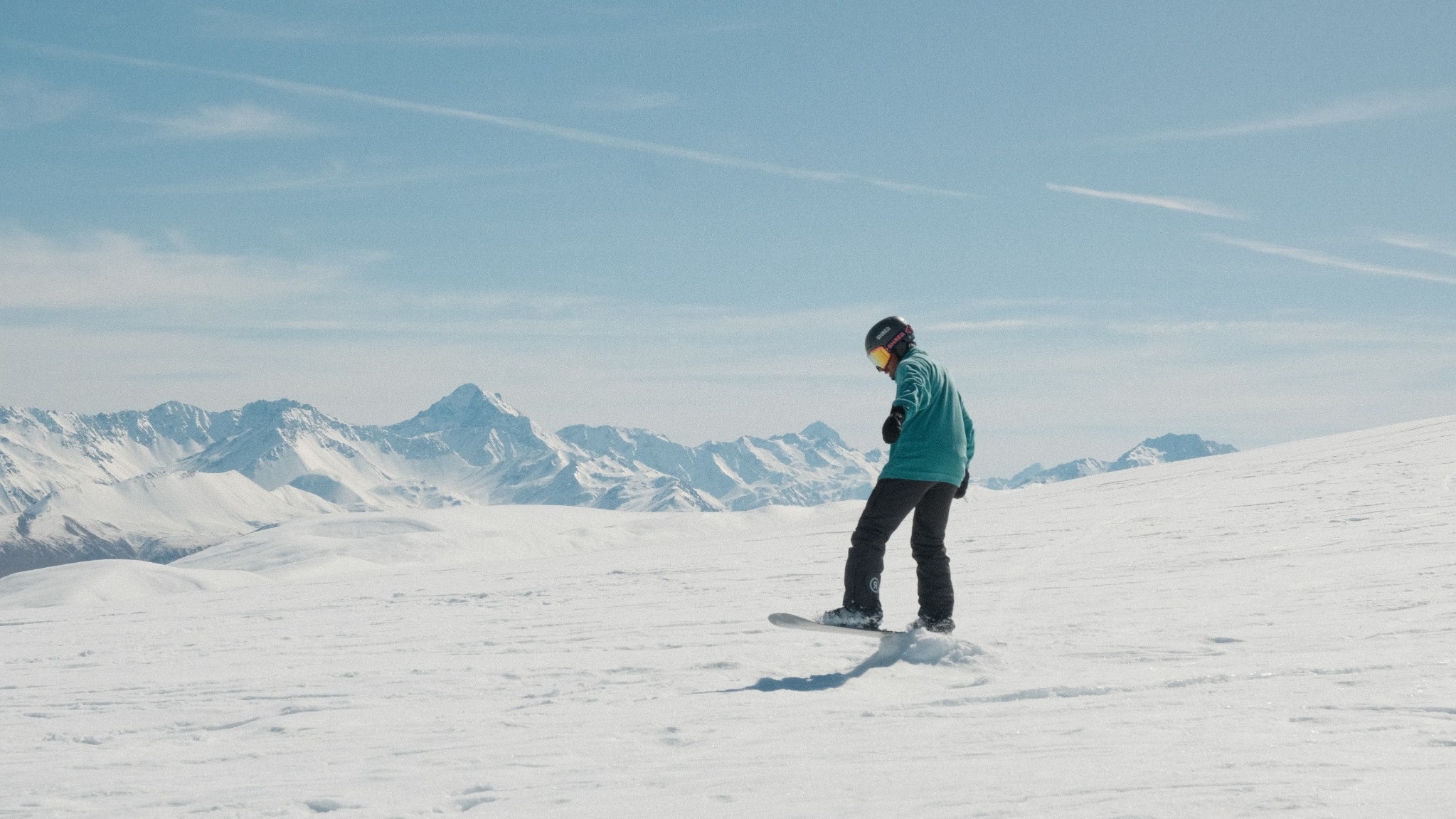Snowboarder mit Helm und Skibrille bei der Abfahrt auf einem verschneiten Hang
