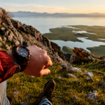 Göl manzaralı yamaçta oturan yürüyüşçünün bileğindeki outdoor spor saatine bakması