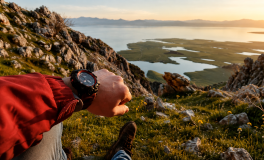 Göl manzaralı yamaçta oturan yürüyüşçünün bileğindeki outdoor spor saatine bakması