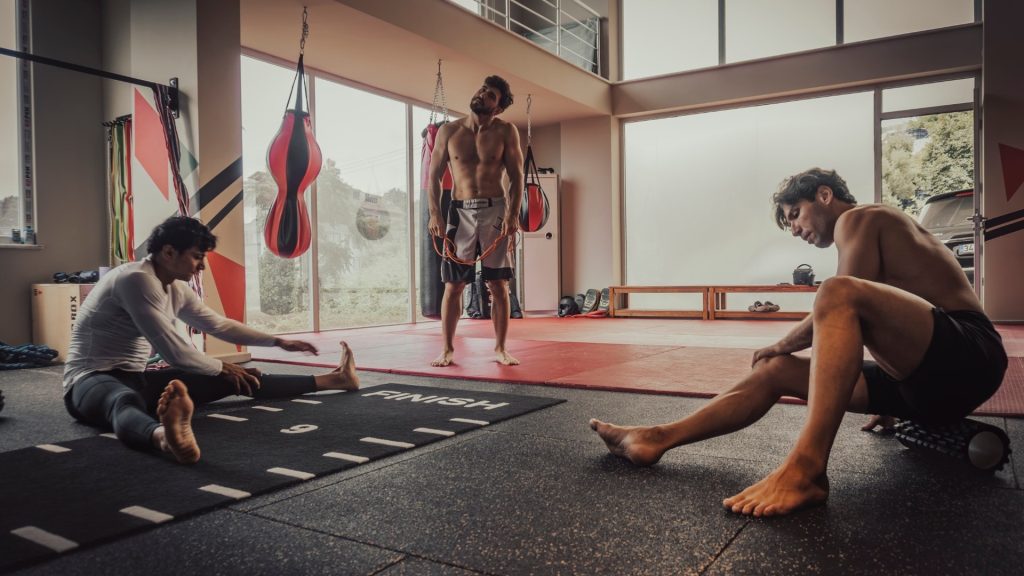 Spor salonunda kuvvet antrenmanı sonrası yerde esneyen ve foam roller kullanan üç sporcu