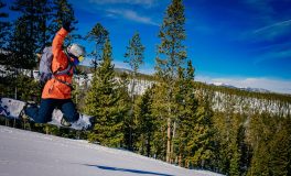 Turuncu montla havalanan snowboardcu; iyi bir kayak kombini mont, pantolon, eldiven ve kask uyumundan oluşuyor