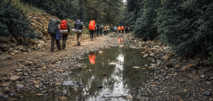 Taşlı patikada, su birikintisinin yanında ıslak zeminde yürüyen sırt çantalı trekking grubu