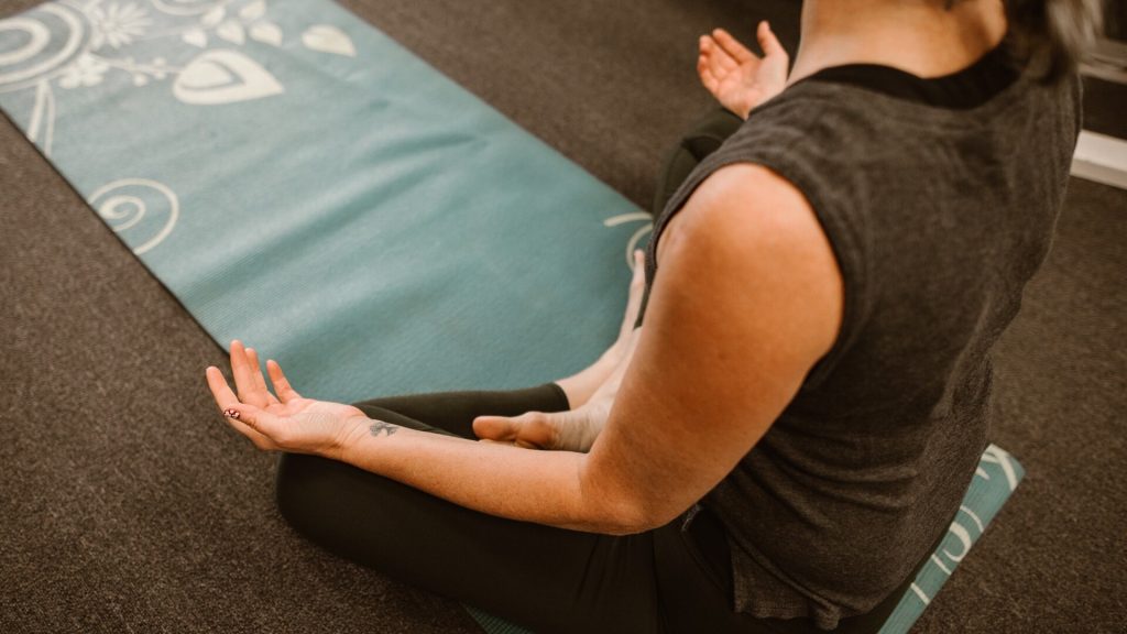 Ağırlık antrenmanı sonrası spor salonu zemininde yoga matının yanında bağdaş kurup oturan kişi