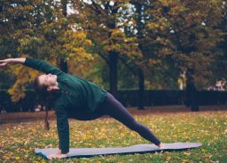 Sonbahar parkında mat üzerinde yan açı pozunda yoga yapan kadın