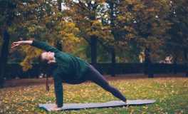 Sonbahar parkında mat üzerinde yan açı pozunda yoga yapan kadın
