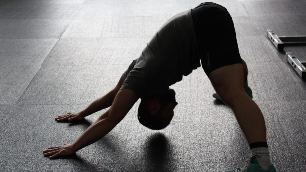 Spor salonunda zeminde aşağı bakan köpek pozunda yoga yapan erkek