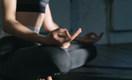 Loş bir salonda bağdaş kurup meditasyon yapan kadın, elleri dizlerinin üzerinde