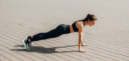Wie macht man Burpees: Frau in der Plank auf gestreckten Armen auf Pflaster, mit gerader Linie vom Kopf bis zu den Fersen
