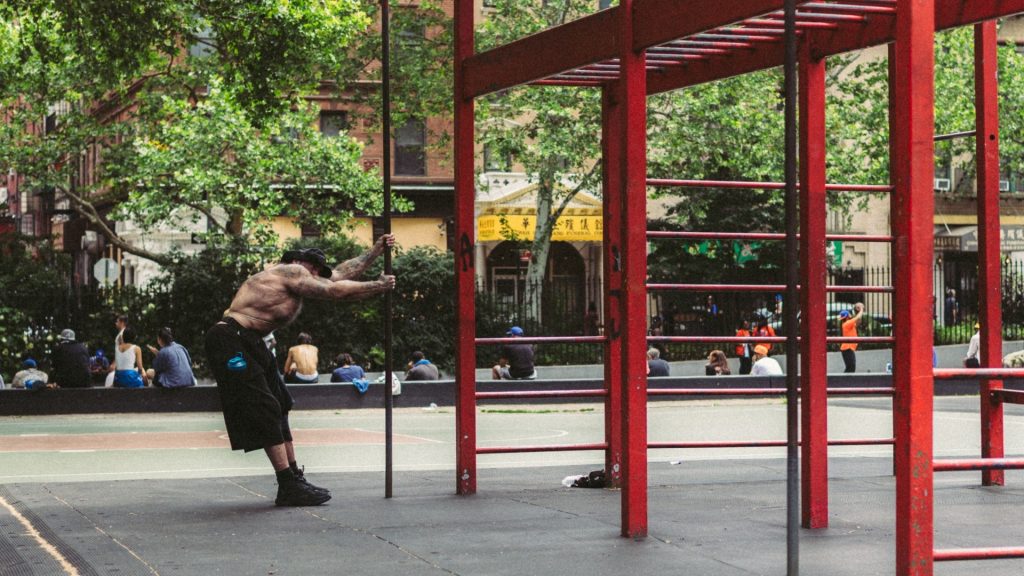 Sportler dehnt sich an einer senkrechten Stange neben roten Klimmzugstangen in einem Calisthenics-Park