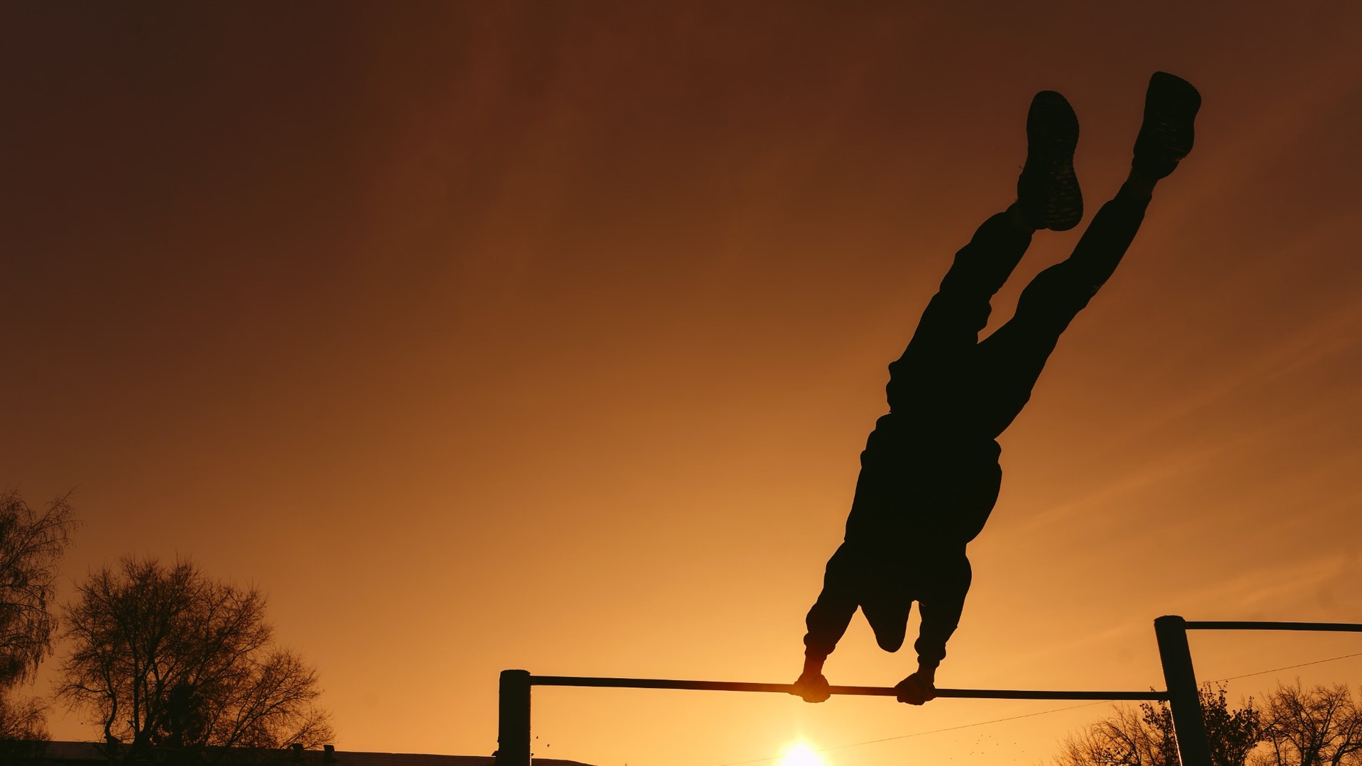 Silhouette eines Sportlers im Handstand auf einer Calisthenics-Stange bei Sonnenuntergang