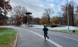 Runner in a jacket, shorts and full-length tights on a park road dusted with snow