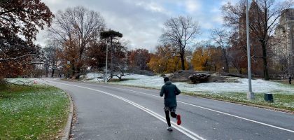 Läufer mit Jacke, Shorts und langen Lauftights auf einer leicht verschneiten Parkstraße
