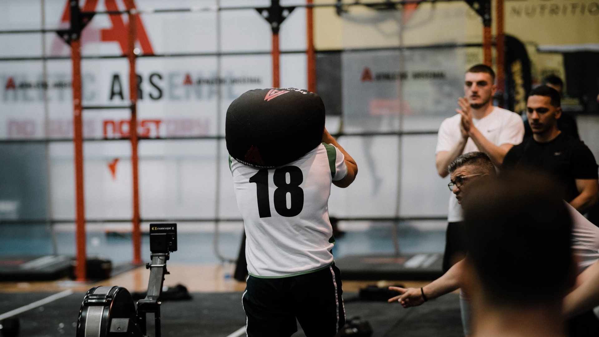 Athlete number 18 starting the sandbag lunge station with a sandbag on his shoulders at a HYROX-style race venue