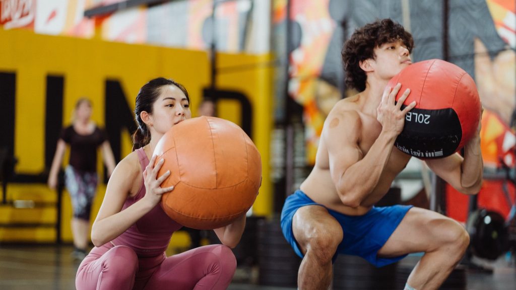 Two athletes in the wall ball squat position, holding medicine balls in front of their chests