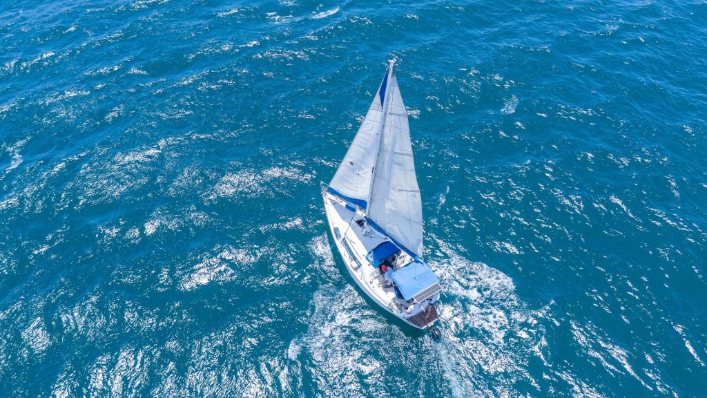 Aerial view of a single-masted sailing boat under sail on a choppy blue sea